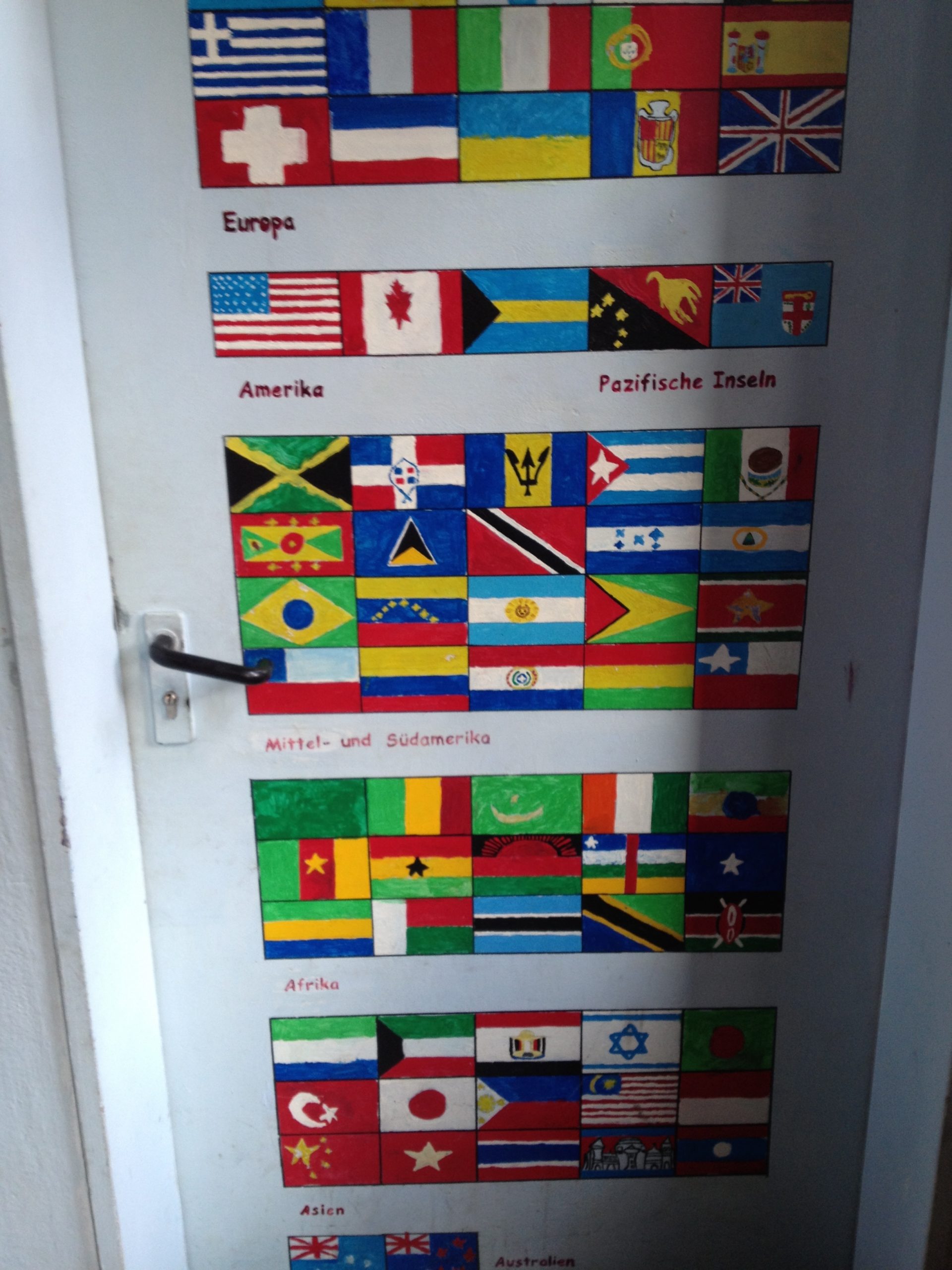 Das Bild zeigt eine Tür mit vielen Flaggen von Nationen rund um den Erdball.
