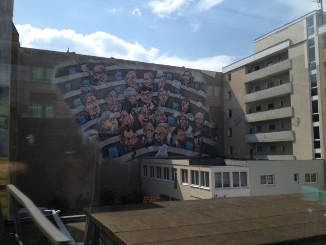 Das Bild zeigt die Bemalung einer Häuserwand in Berlin, mit den Rängen des Dt. Bundestages.