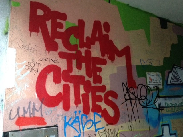 Das Foto zeigt den Schriftzug "Reclaim the Cities" als Grafiti an einer Häuserwand.