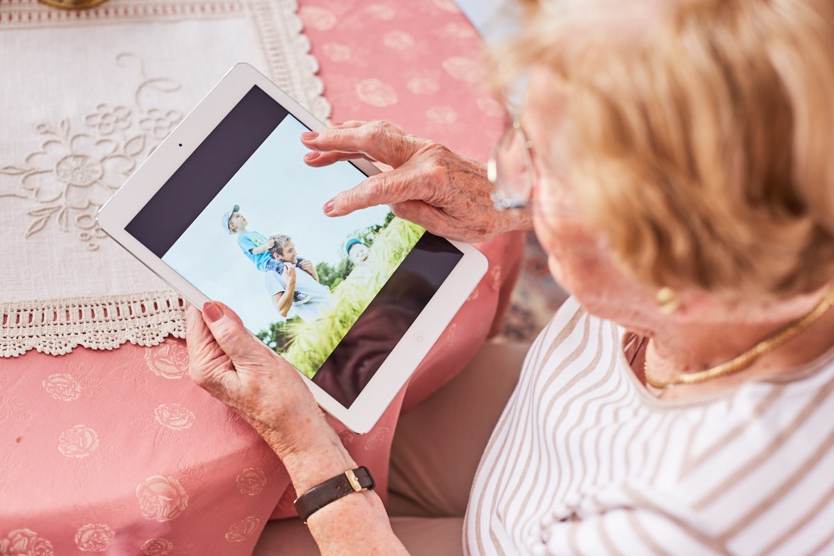 Blick aus der Vogelperspektive auf eine ältere Frau, die ein Tablet in der Hand hält.