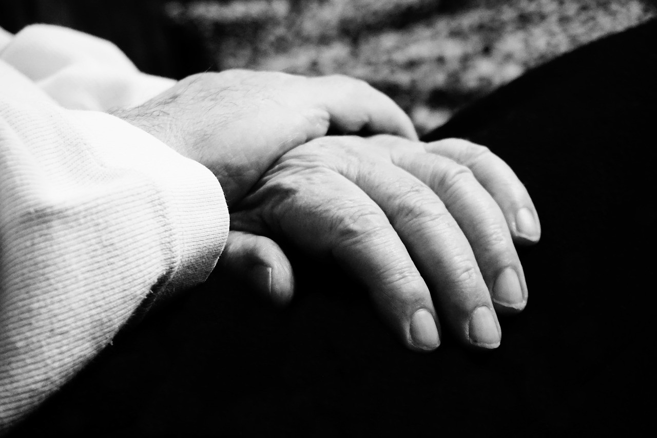 Schwarz-weiß Foto. Eine etwas jüngere Hand greift nach der Hand einer älteren Person.